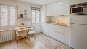 A kitchen with white cabinets, a microwave, a refrigerator, a window with blinds, and a radiator. - Apartment 'Loló Vut' with Wi-Fi (Burgos)