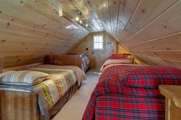 A cozy attic bedroom with two beds, wooden walls, and a small window.