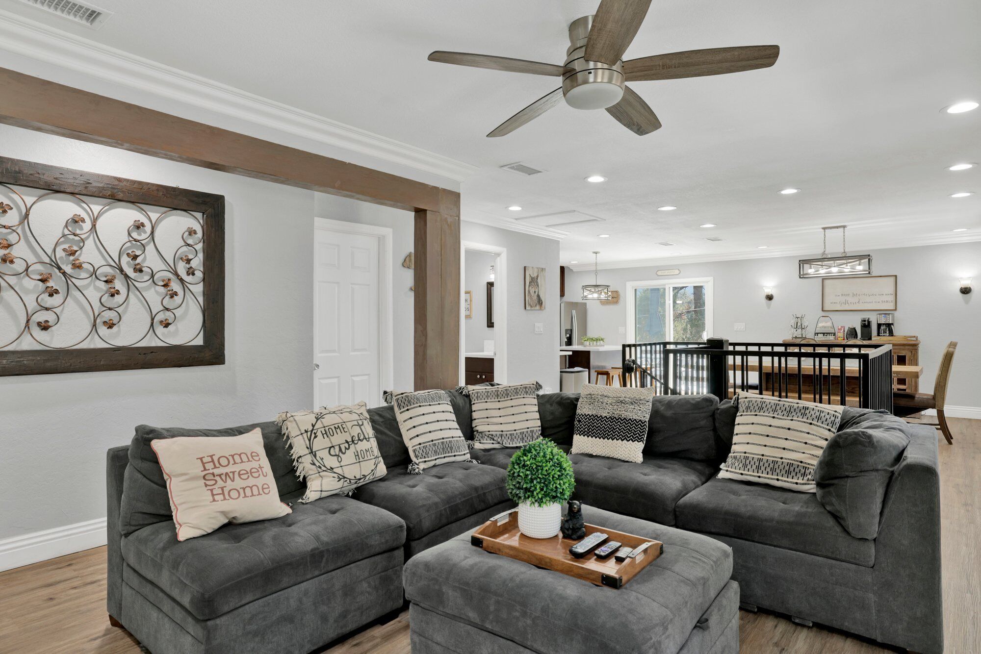 A modern living room with a gray sectional sofa, a ceiling fan, and a dining area in the background.