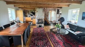 Un amplio salón con una mesa de comedor de madera, sofás negros y una chimenea.