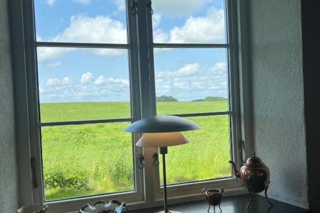 Een kamer met een groot raam, met uitzicht op een groen veld en een heldere lucht.