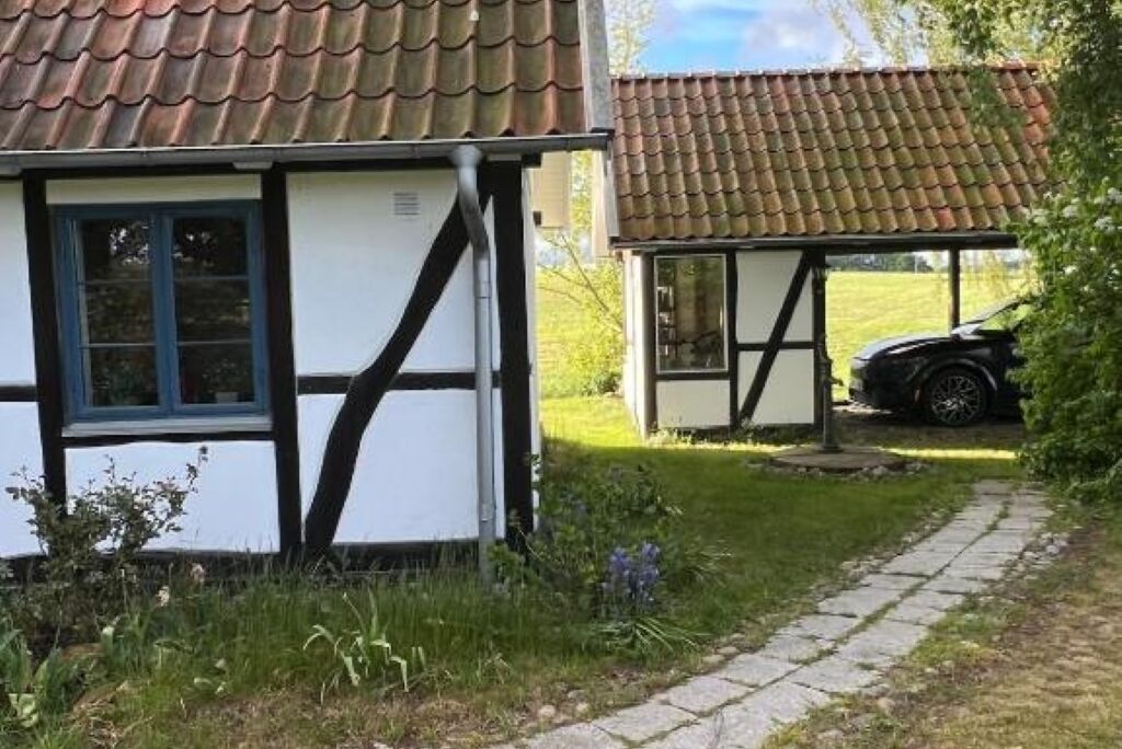 En traditionell byggnad med korsvirkesfasad och ett tak täckt med tegelpannor, en stenlagd gångväg och en parkerad bil.