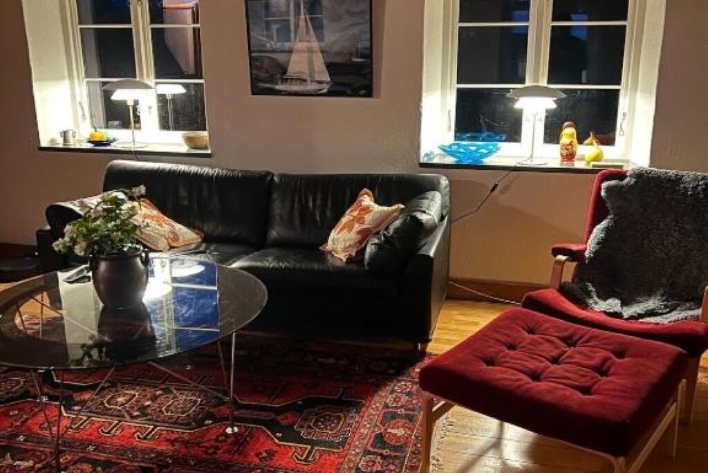 Un salon avec un canapé en cuir noir, un fauteuil rouge, une table basse en verre et un tapis à motifs.