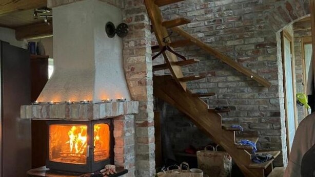 A rustic stone fireplace with a chimney, wooden beams, and a staircase leading to an upper level. - Renovated Half-timbered house in Österlen built 2006 (Skåne län)