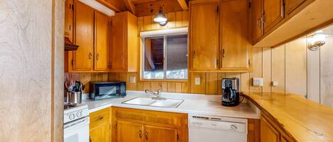 Una cocina compacta con armarios de madera, una estufa blanca, un microondas y un lavavajillas.