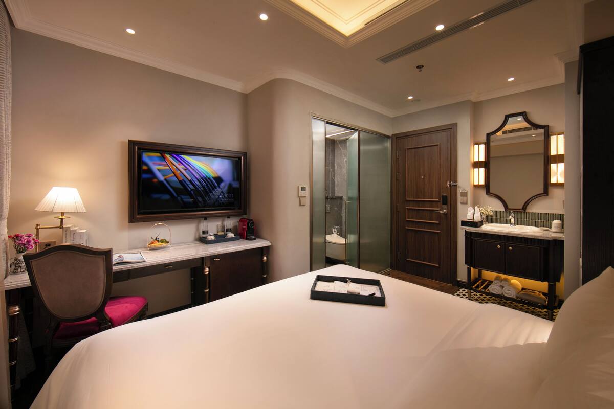 Hotelkamer met een bed, een bureau met een computer, een televisie, een badkamer met een spiegel en een deur.