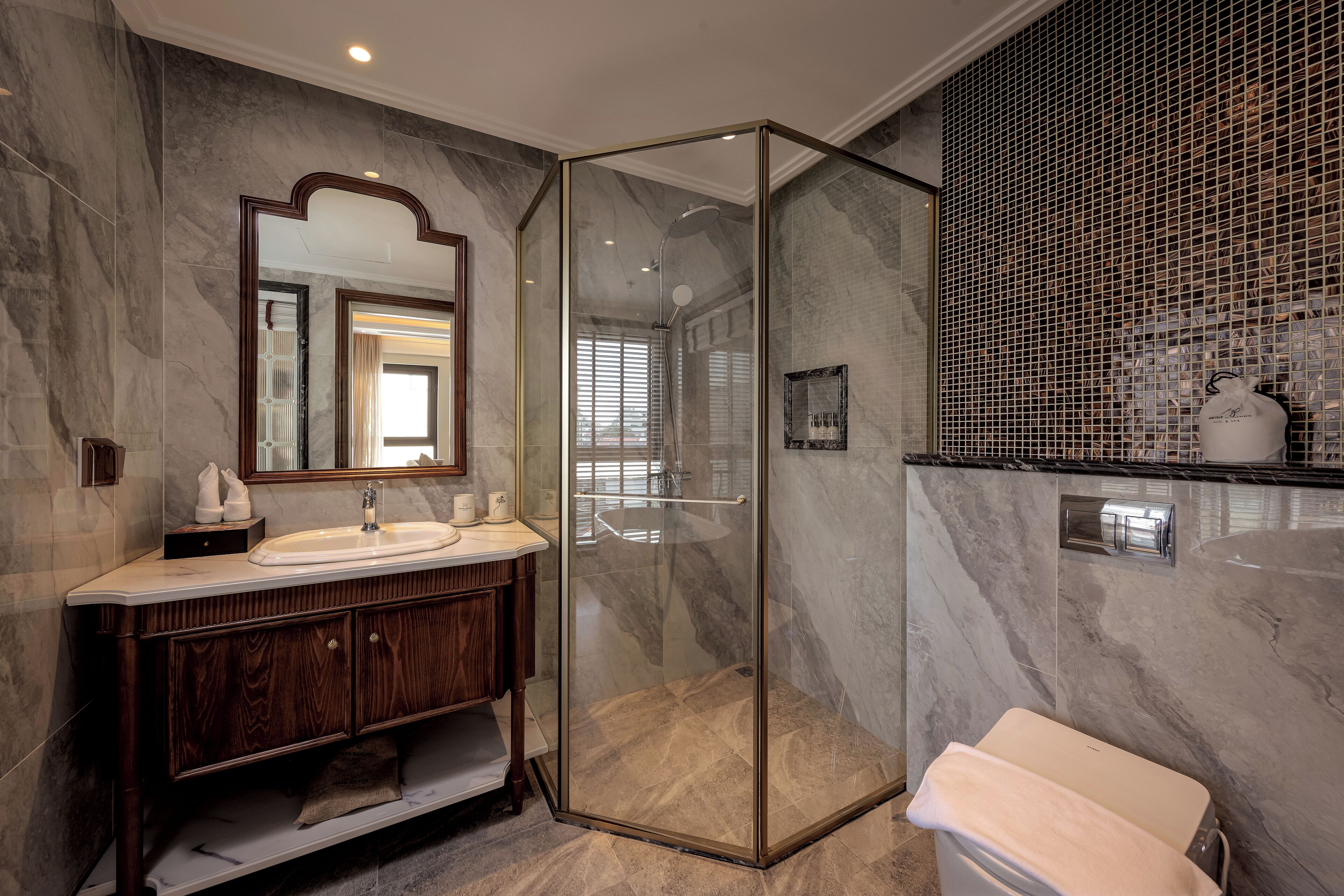 Une salle de bain moderne avec un meuble-lavabo en marbre, une douche à parois de verre et un mur recouvert de carreaux formant un motif décoratif.