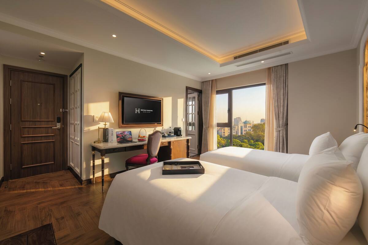 Een hotelkamer met twee bedden, een bureau met een televisie, uitzicht op de stad en een houten vloer.