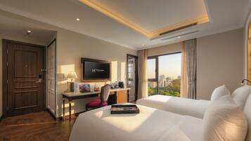 Ein Hotelzimmer mit zwei Betten, einem Schreibtisch mit Fernseher, Blick auf die Stadt und Holzboden.