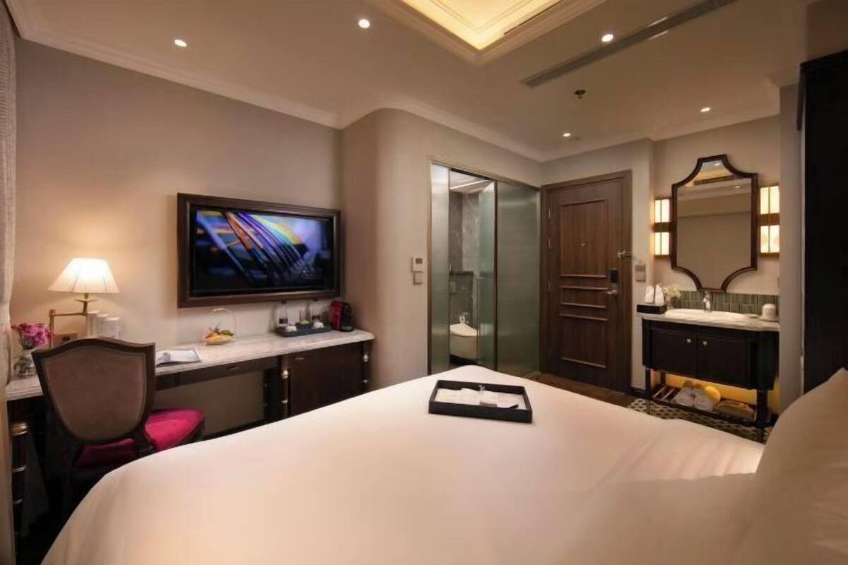 Een hotelkamer met een bed, een bureau met een computer, een televisie, een spiegel en een deur naar de badkamer.