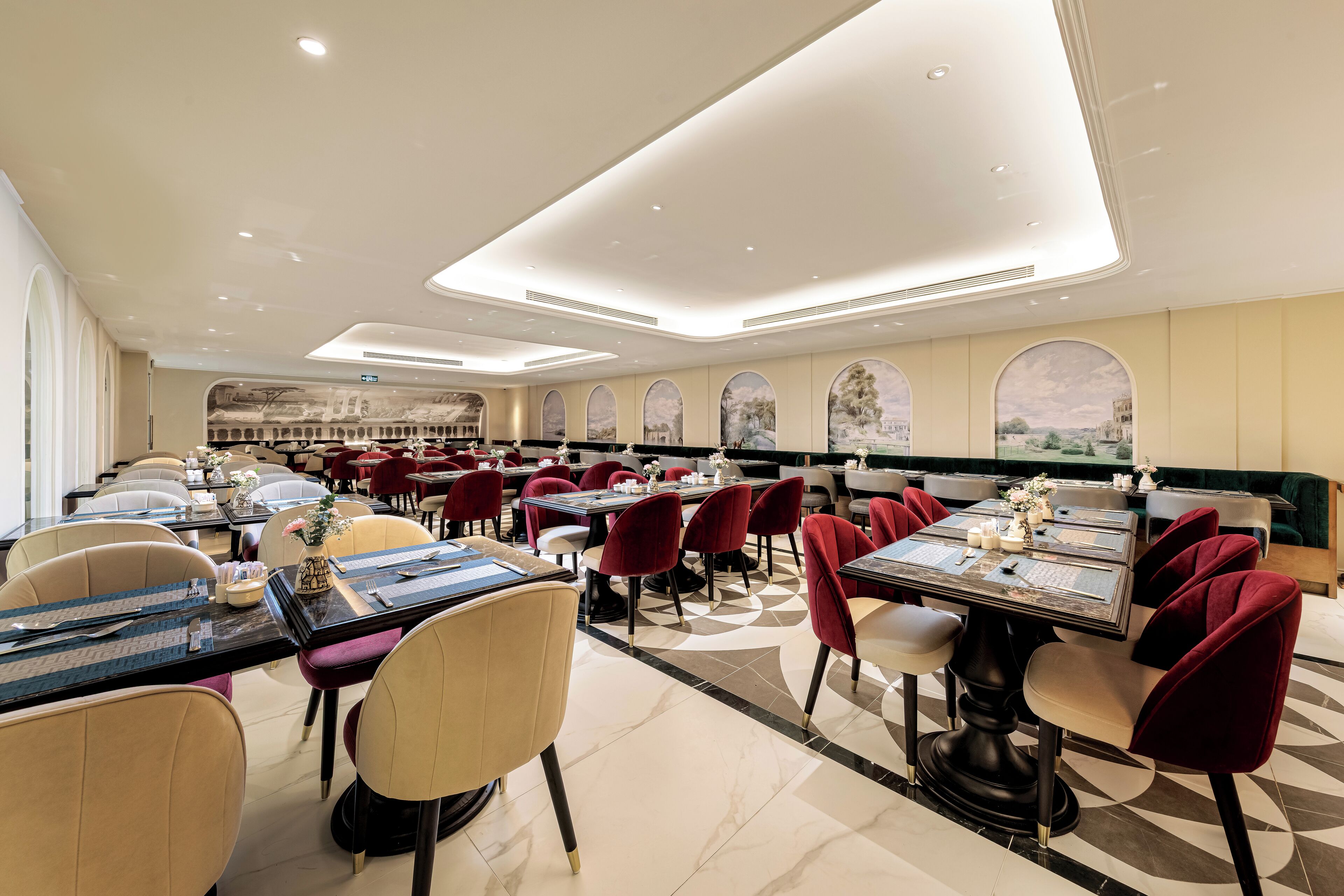 A spacious restaurant with multiple dining tables and chairs, featuring a modern ceiling design and large windows with scenic views.
