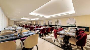 A spacious restaurant with multiple dining tables and chairs, featuring a modern ceiling design and large windows with scenic views.