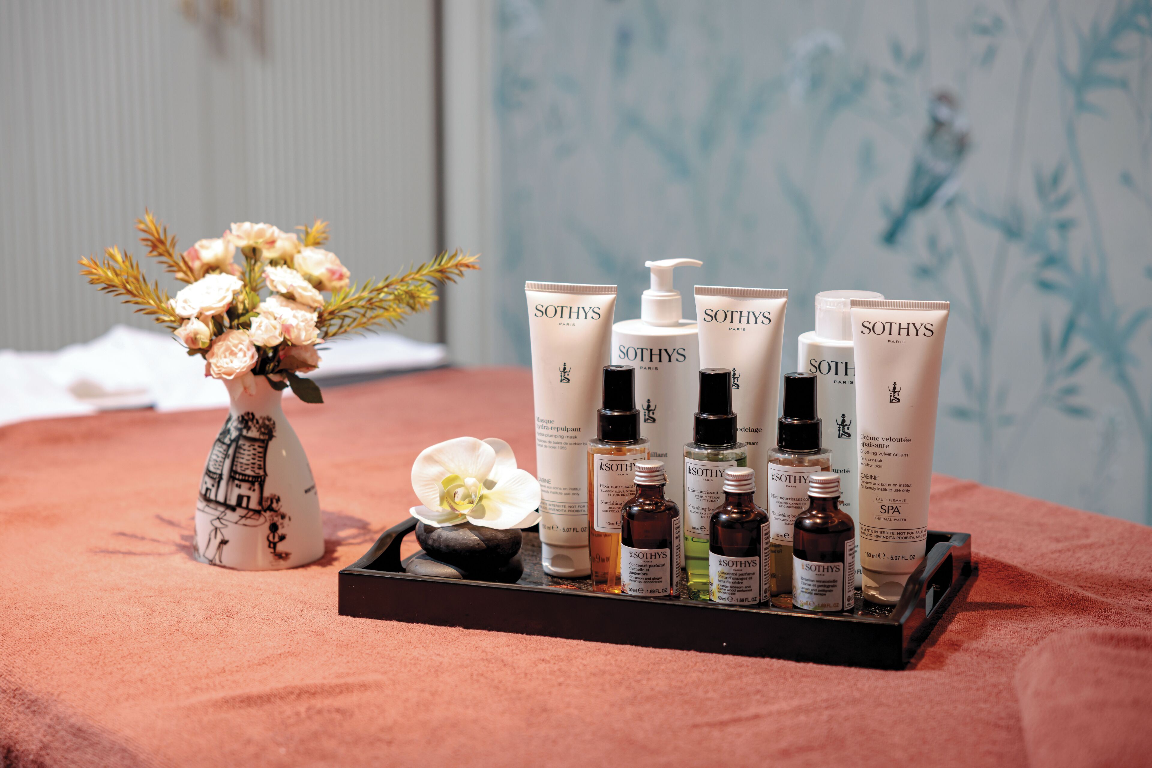 A tray with various Sothys Paris skincare products and a vase with flowers on a textured surface.