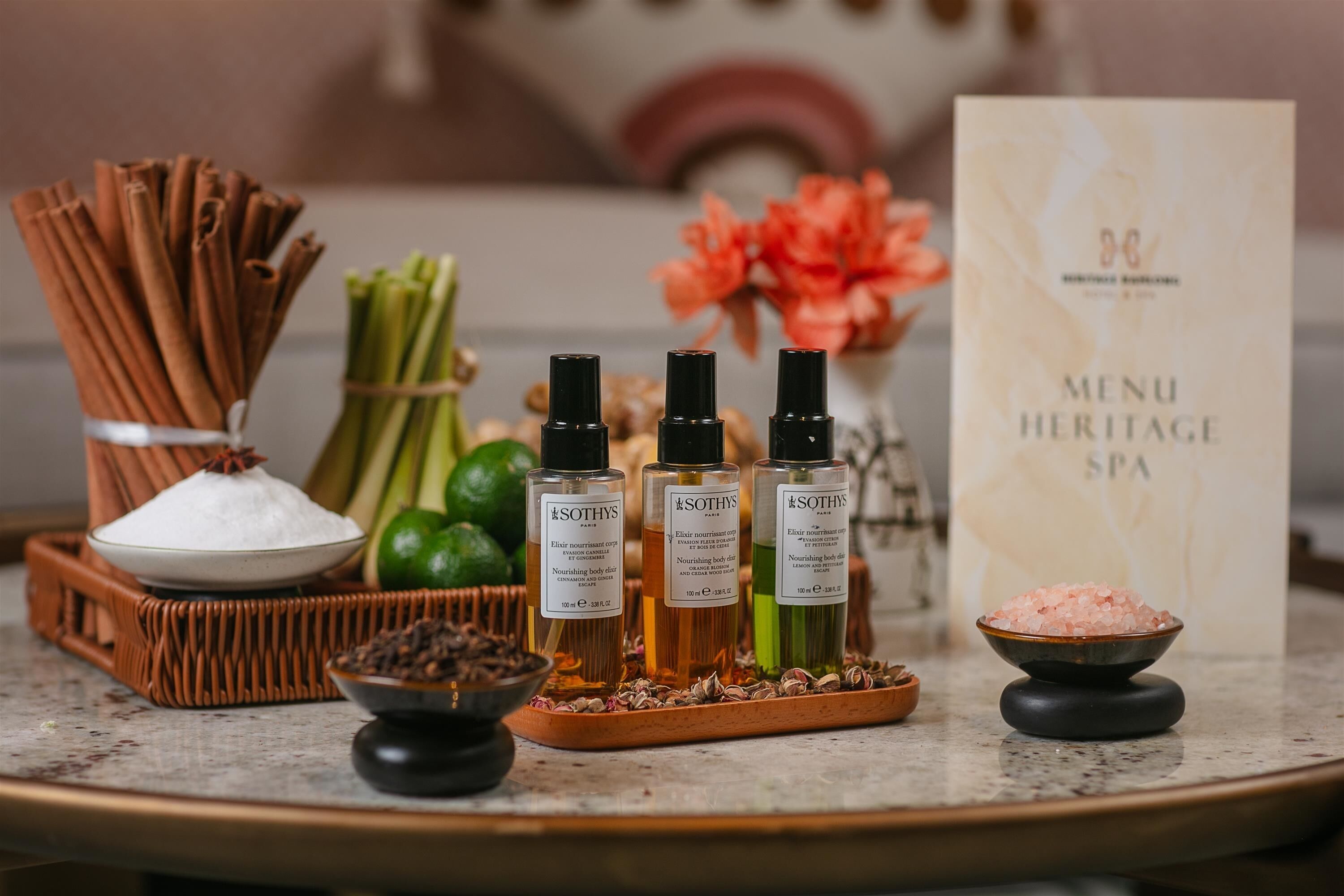 A spa menu board, three bottles of Sothys body care products, a bowl of pink bath salts, and a tray with various bath products.