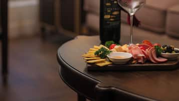 A dining table with a bottle of wine, a glass, and a variety of cheeses and fruits.