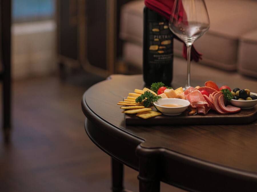 A dining table with a bottle of wine, a glass, and a variety of cheeses and fruits.