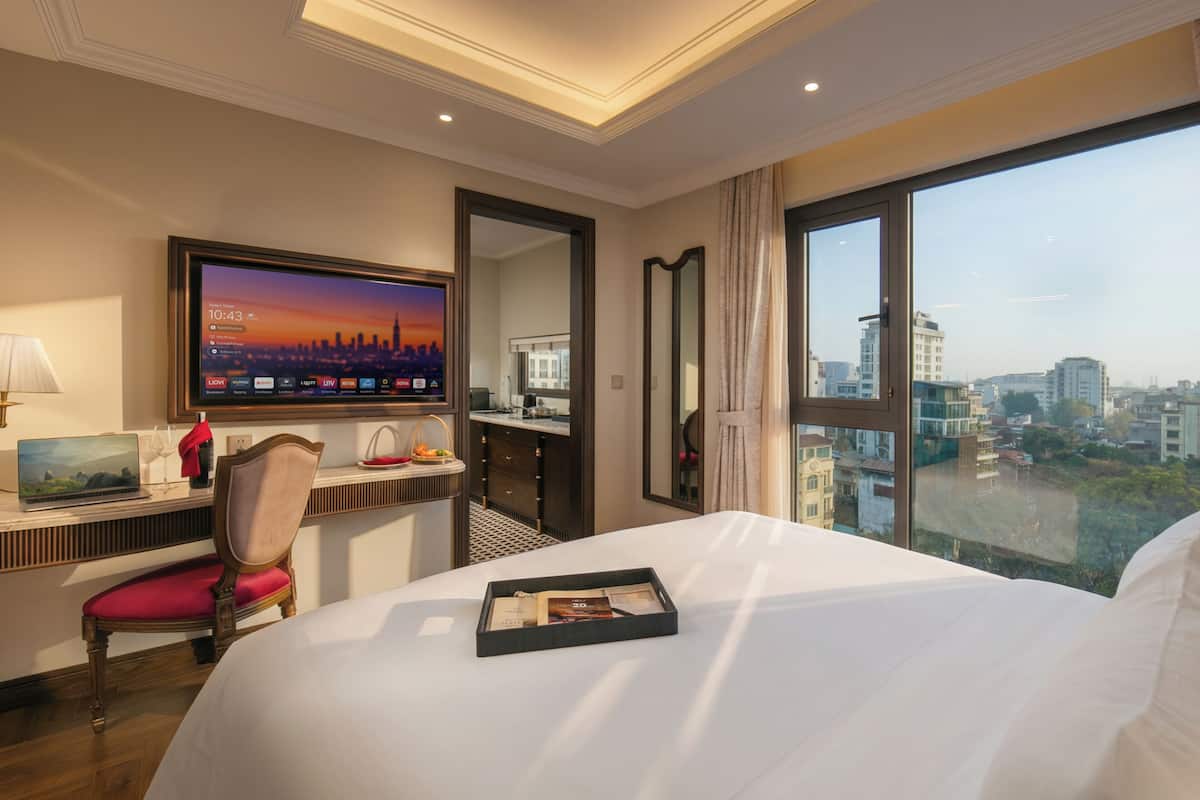Een hotelkamer met een bed, een bureau met een laptop, een televisie en uitzicht op de stad.
