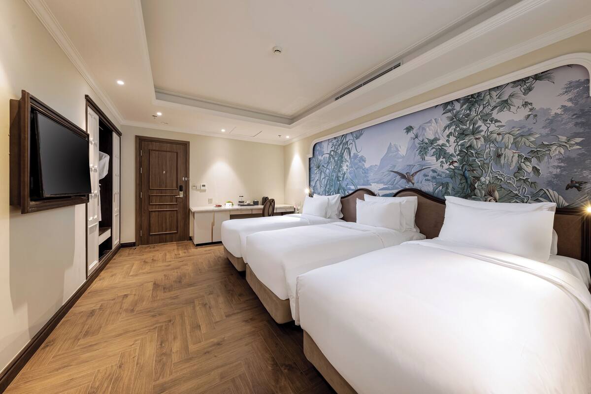 Een hotelkamer met twee bedden, een bureau, een televisie en een muurschildering.
