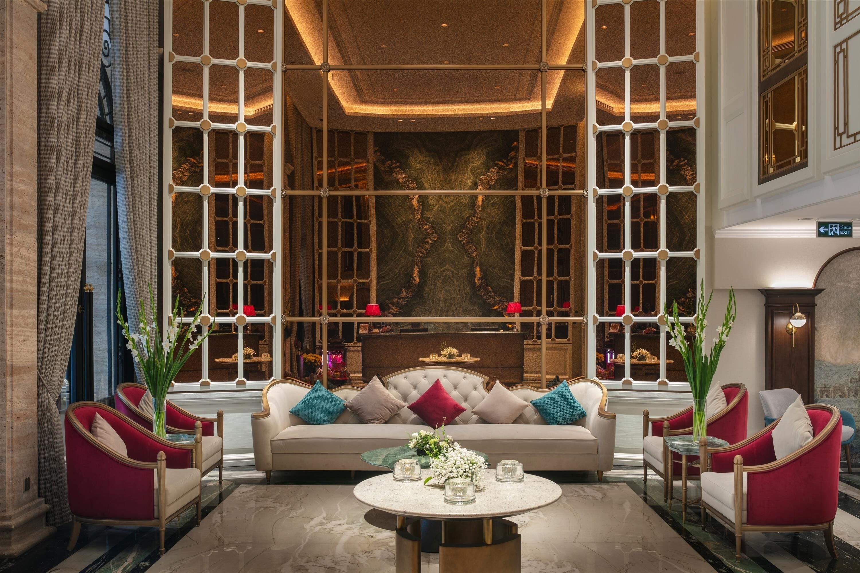 Eine luxuriöse Lobby mit einer zentralen Couch, roten Sessel und einem Marmortisch, sowie einer Wand mit einer Chandelier-Beleuchtung.
