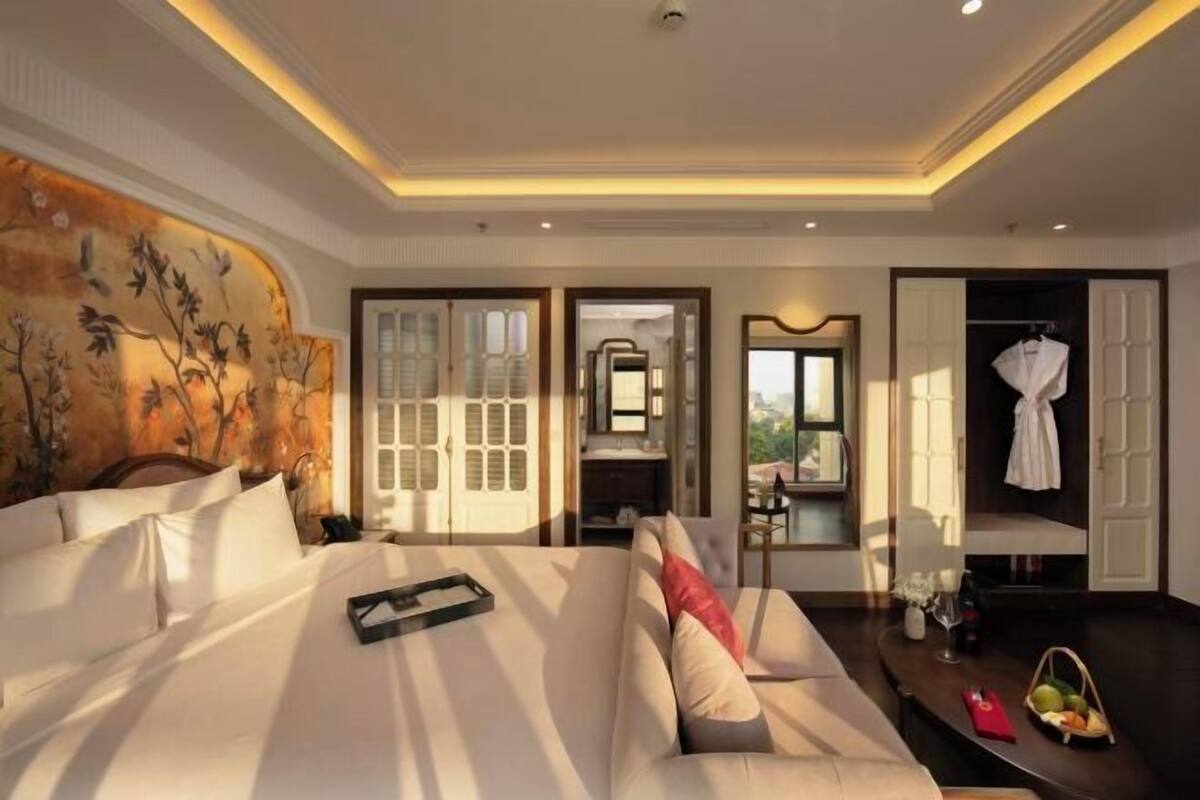 Een hotelkamer met een bed, een bank, een zithoek en een badkamer zichtbaar door een geopende deur.