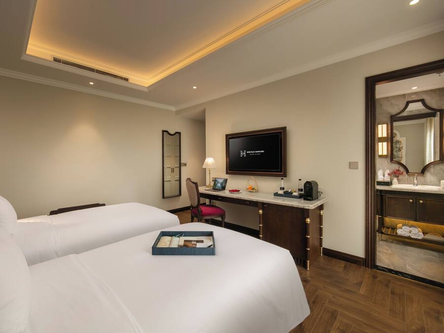 Une chambre d’hôtel avec deux lits, un bureau avec un ordinateur, une télévision et une salle de bain équipée d’un miroir et d’un porte-serviettes.