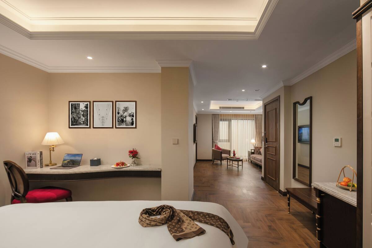 Een hotelkamer met een bed, bureau, stoel, lamp en beelden in lijsten aan de muur.