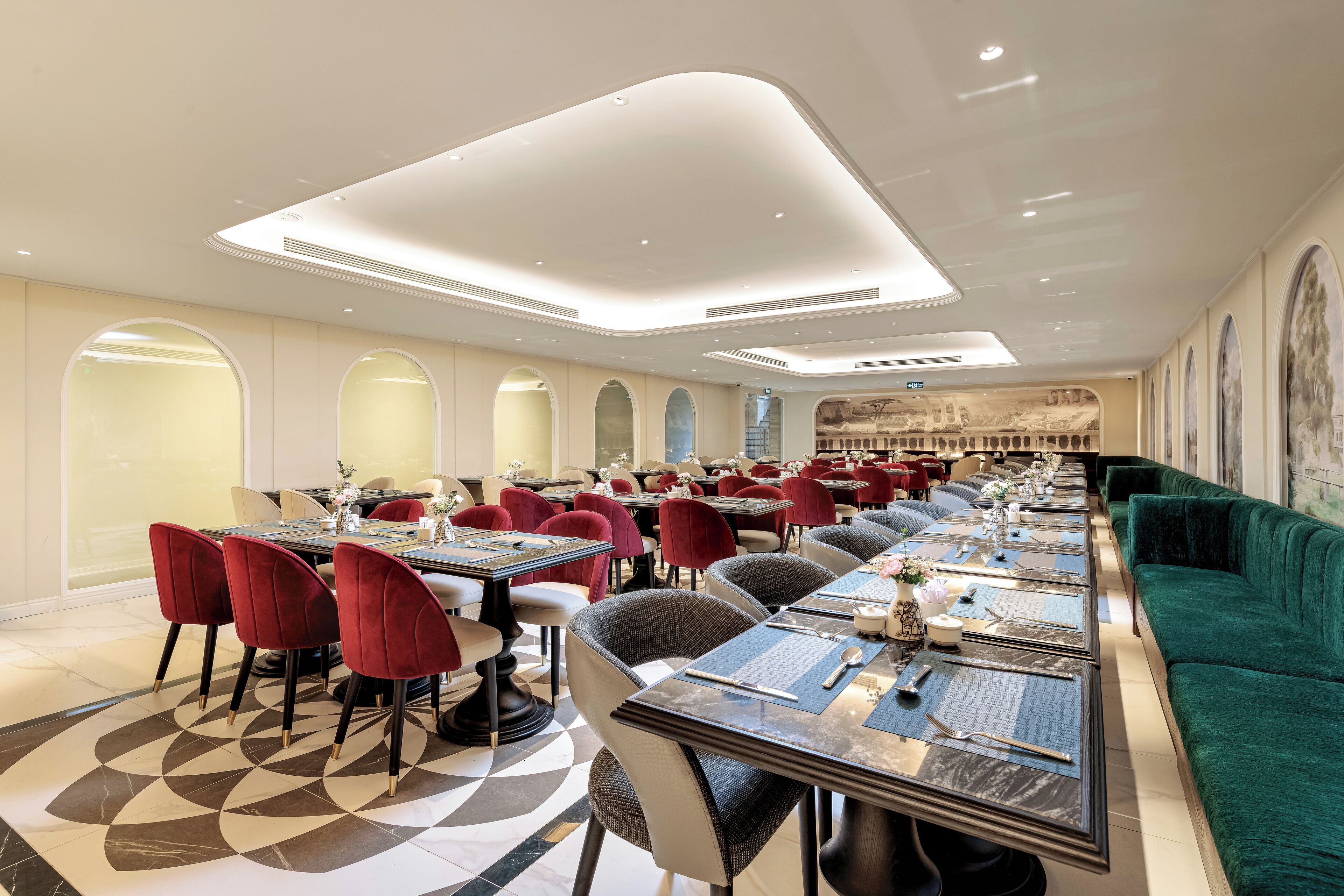 Ein geräumiges Restaurant mit mehreren Esstischen, roten und grauen Stühlen sowie einer grünen Couch.