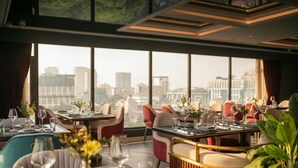 Ein Restaurant mit gedeckten Tischen, großen Fenstern mit Blick auf die Stadt und modernem Interieur.
