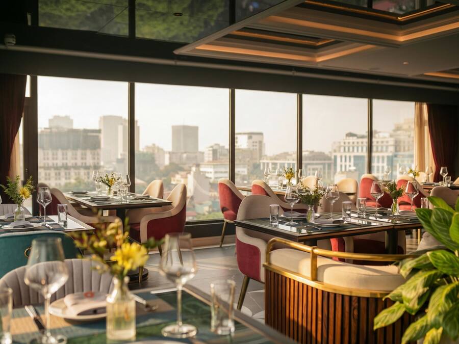 A restaurant with tables set for dining, large windows offering a city view, and modern interior design.