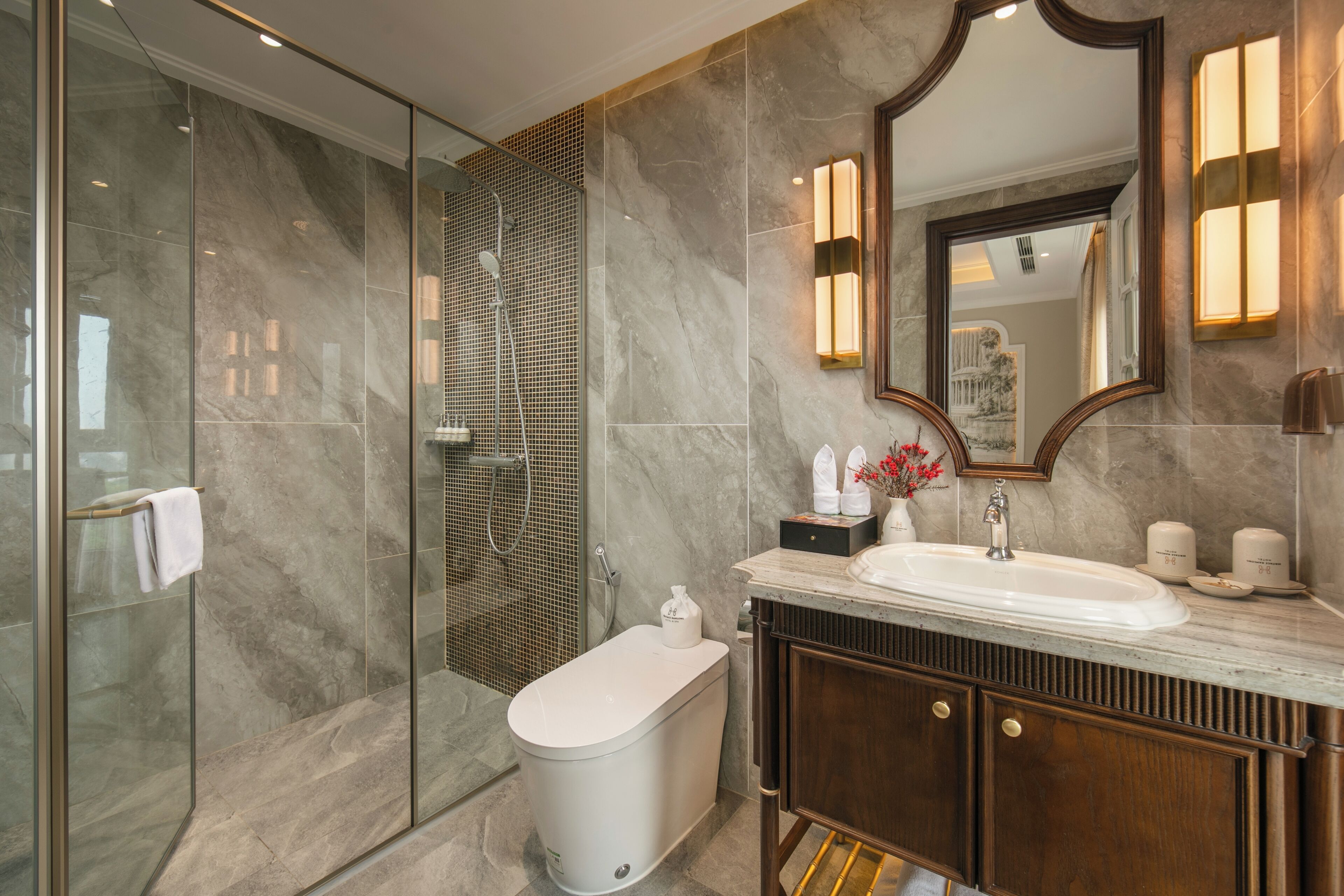 A modern bathroom with a glass-enclosed shower, a freestanding bathtub, a vanity with a mirror, and a marble-tiled wall.
