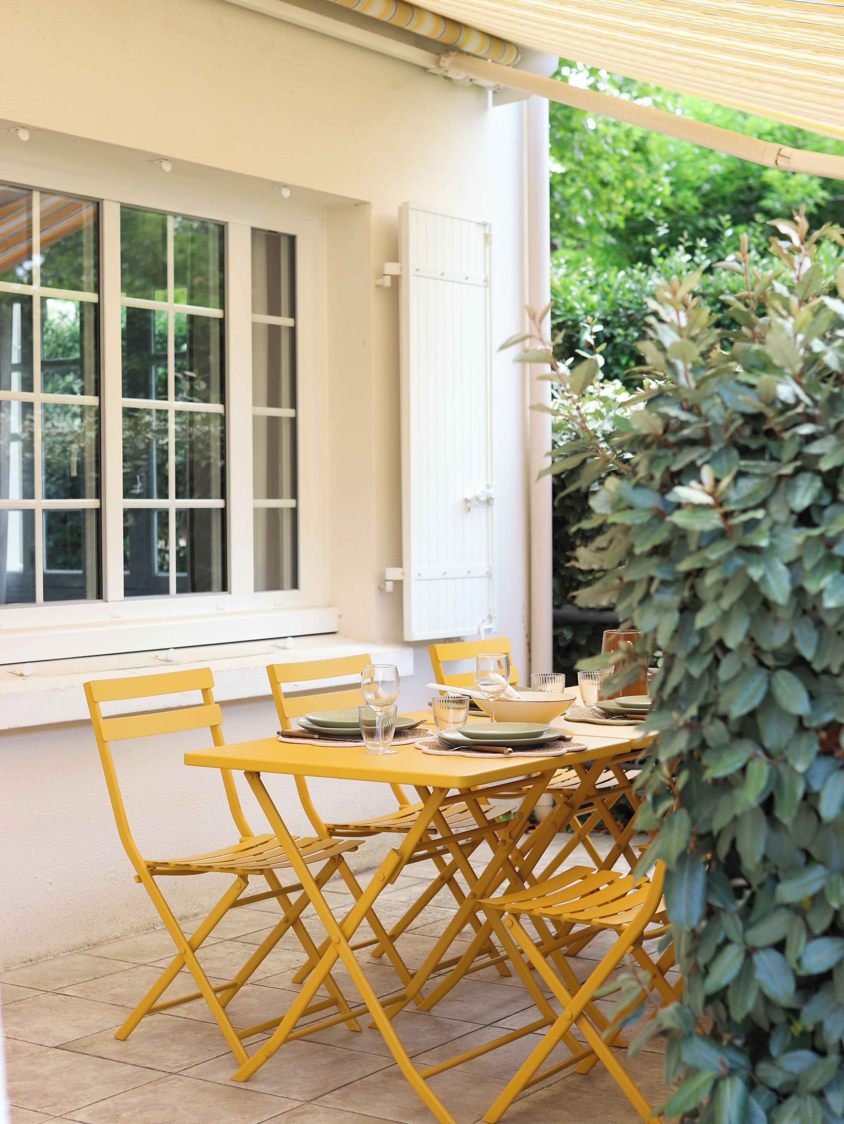 Un comedor con sillas amarillas y una mesa dispuesta para cuatro personas, una puerta blanca y una ventana con persianas.