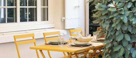 Un comedor con sillas amarillas y una mesa dispuesta para cuatro personas, una puerta blanca y una ventana con persianas.