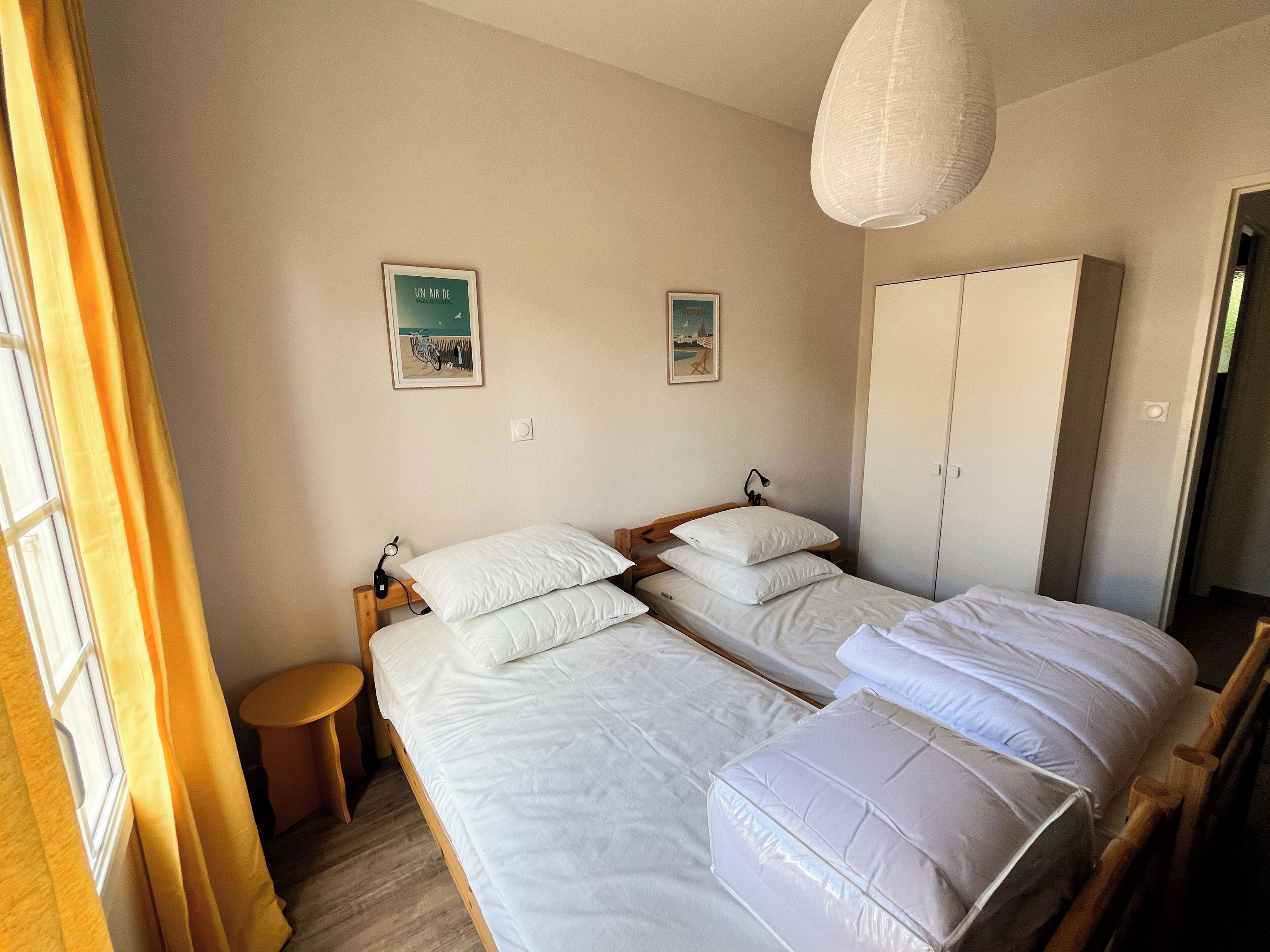 Une chambre avec deux lits, une armoire et deux tableaux accrochés au mur.