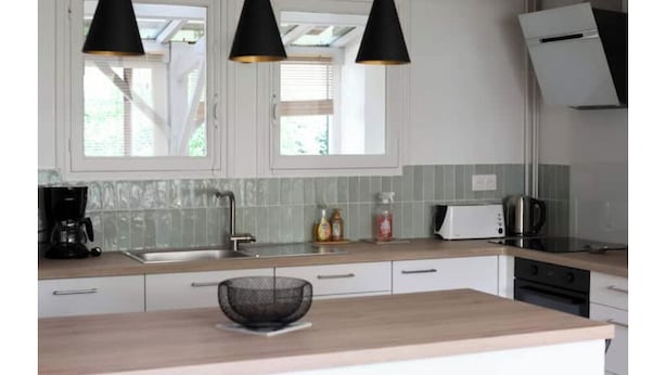 Une cuisine moderne avec des meubles blancs, un plan de travail en bois, une machine à café, un grille-pain et des suspensions noires.