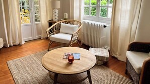 Une pièce chaleureuse avec un fauteuil en osier, une table ronde en bois et une vue sur la verdure grâce à de grandes fenêtres.