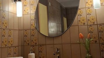 Ein Badezimmer mit einem runden Spiegel, zwei Wandleuchten, einem Waschbecken, einem Handtuch und einer Vase mit Blumen.