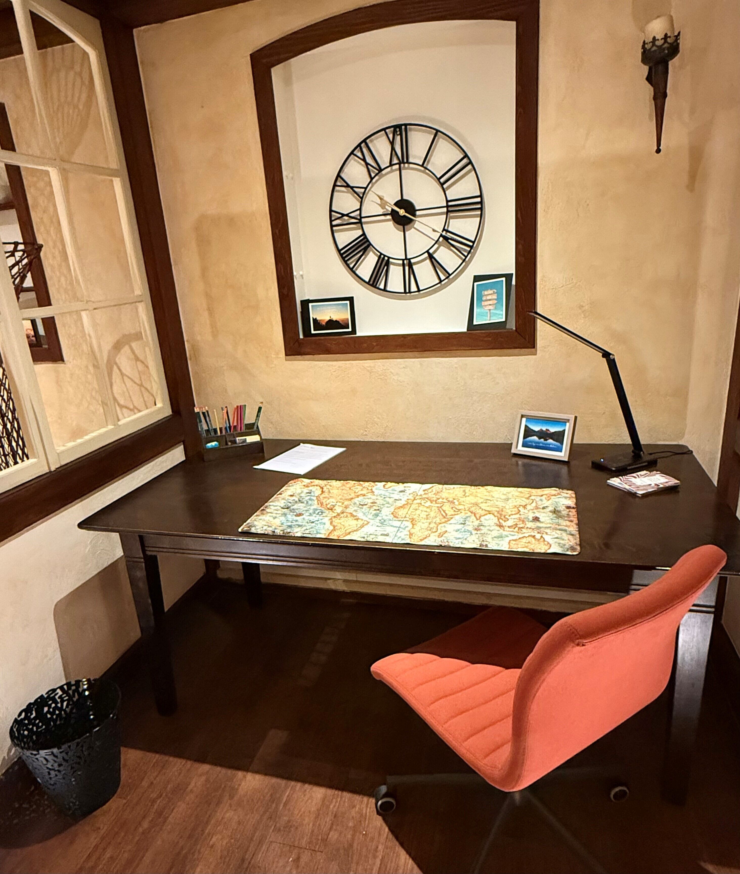 A desk with a world map, a clock, and a lamp.