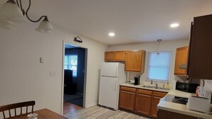 A kitchen with wooden cabinets, a white refrigerator, a microwave, and a toaster. There is a dining table with chairs and a small decorative vase. - Clean Spacious 3BR, ½ Mi to Hospital, Near Universities, Fast WiFi, Pet-Friendly (Princeton)