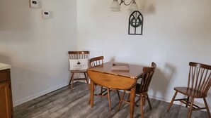 A dining area with a wooden table and four chairs, a chandelier, and a wall-mounted wreath. - Clean Spacious 3BR, ½ Mi to Hospital, Near Universities, Fast WiFi, Pet-Friendly (Princeton)