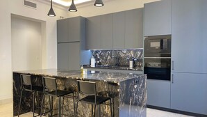 Una cocina moderna con una isla de mármol, taburetes de bar, armarios grises y electrodomésticos integrados.