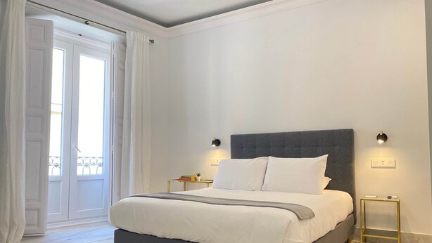 Un dormitorio moderno con una cama grande, dos mesitas de noche y vistas al balcón exterior.