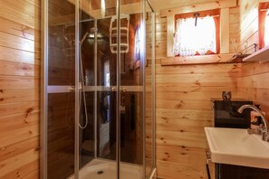 A wooden cabin bathroom with a glass-enclosed shower, a sink, and a window with lace curtains. - Holiday Homes, Summer Pool, Whirlpool, Sauna (Mielno)