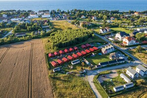 An aerial view of a coastal village with residential buildings, a large field, and a forested area. - Holiday Homes, Summer Pool, Whirlpool, Sauna (Mielno)