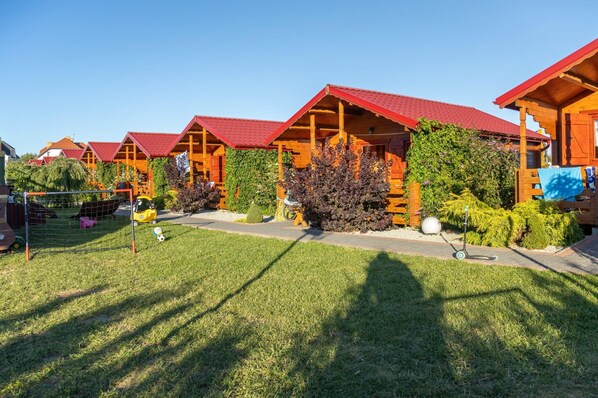 A row of wooden cabins with red roofs, surrounded by well-maintained lawns and greenery. - Holiday Homes, Summer Pool, Whirlpool, Sauna (Mielno)