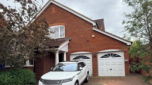 A house with a brick exterior, a white car parked in the driveway, and two garage doors. - Nice 1-bedroom apartment in Milton Keynes (Milton Keynes)