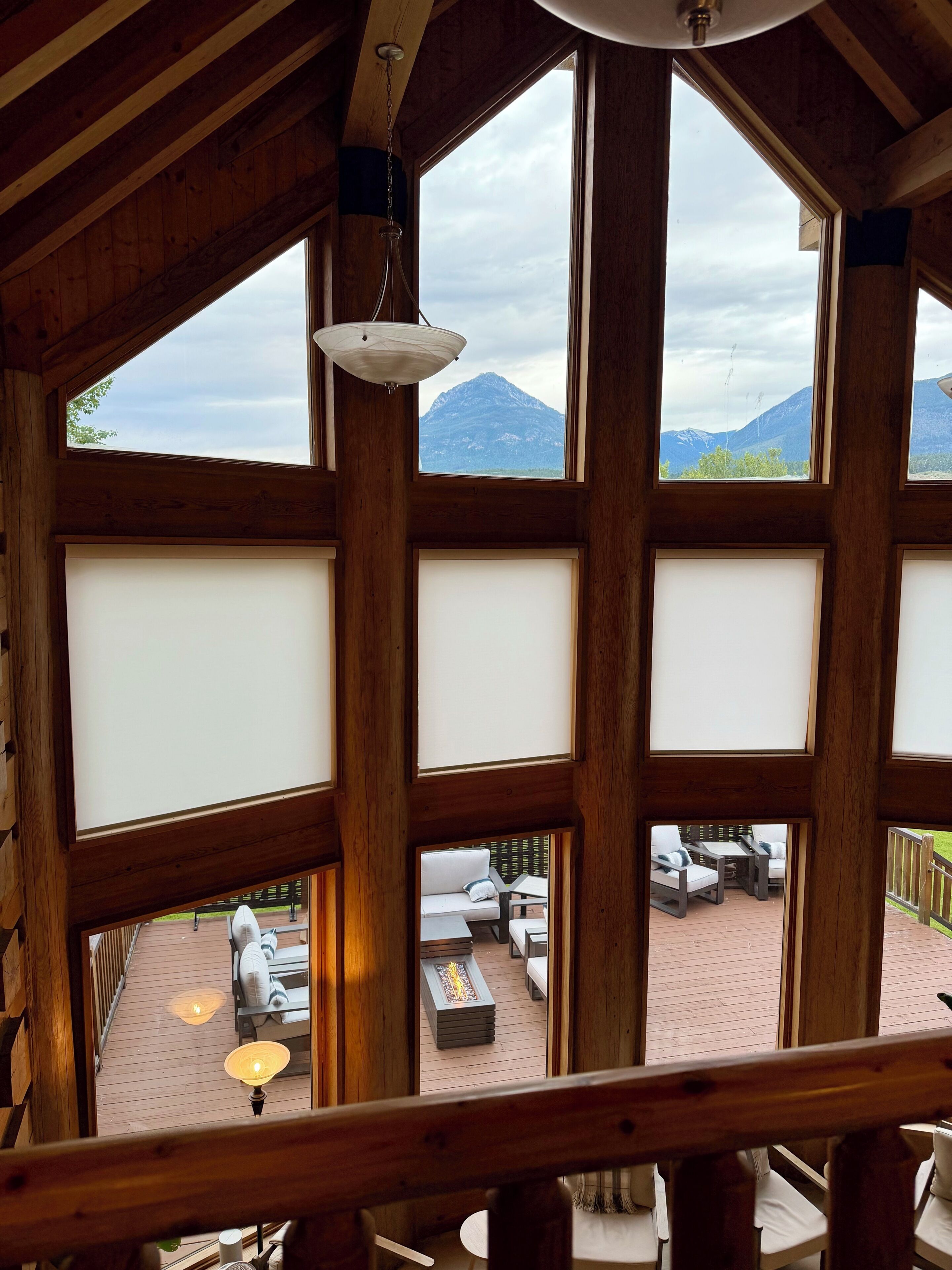 A wooden interior with large windows overlooking a deck area with outdoor seating.