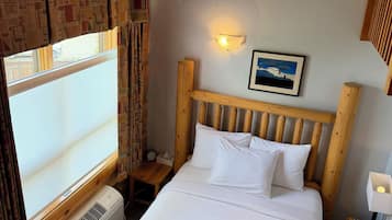 Habitación de hotel con cama, mesita de noche, luz de pared, cuadro enmarcado y ventana con cortinas.