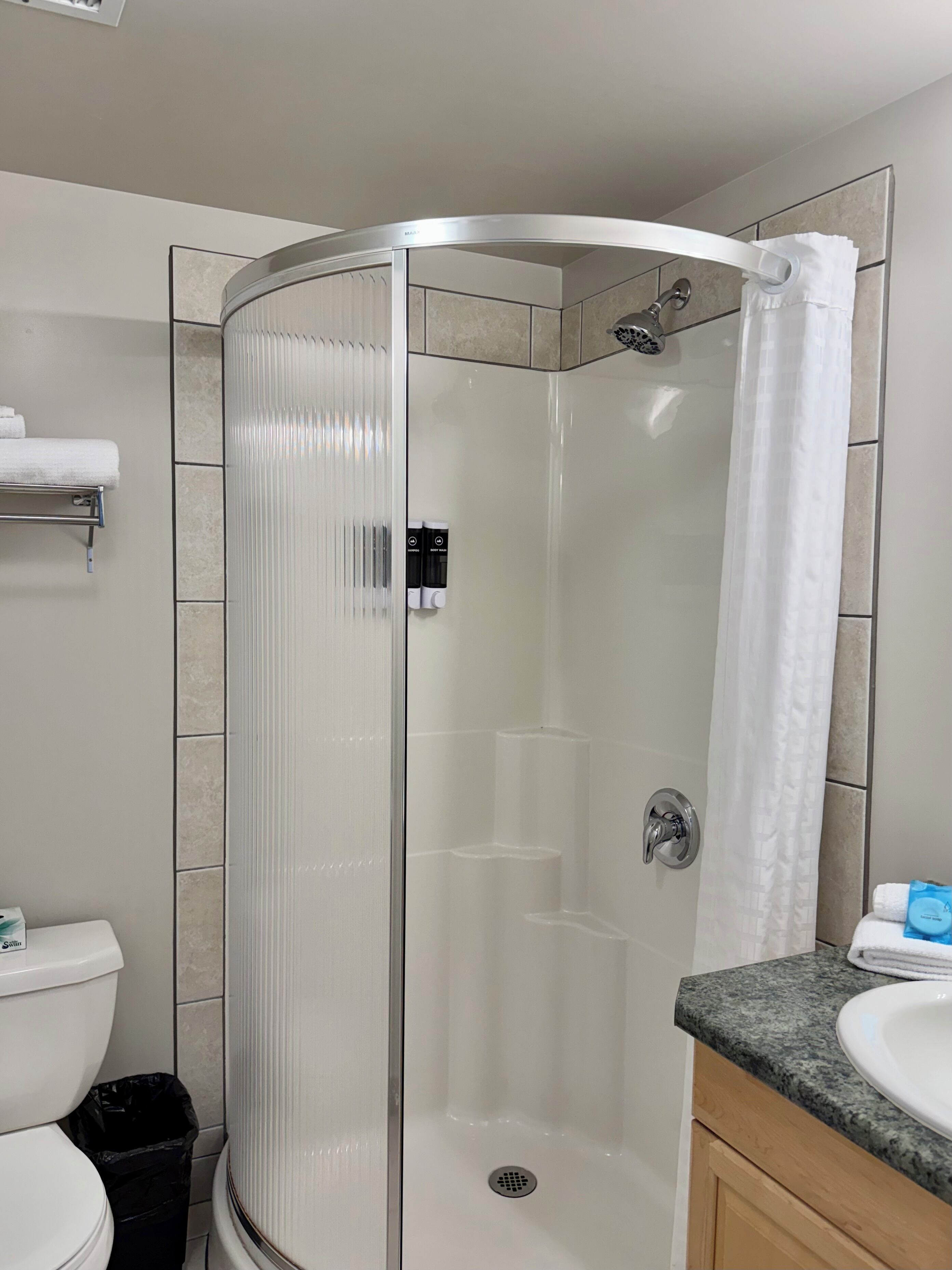 Un baño moderno con ducha de vidrio, inodoro y lavamanos con encimera de granito.