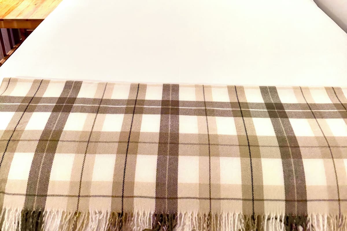 Un dormitorio con cama, almohadas, cabecera de madera, mesita de noche con lámpara y estante de madera en la pared.