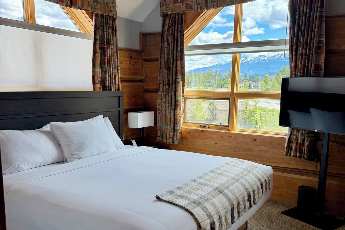 Habitación de hotel con una cama grande, televisión, ventana con vistas a la montaña y paredes de madera.